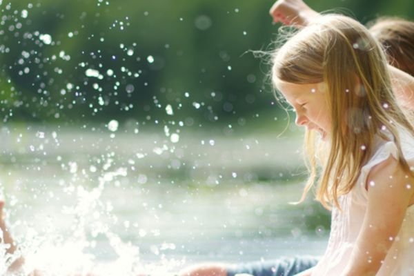 Two cute little girls sitting on a wooden platform by the river or lake dipping their feet in the water on warm summer day